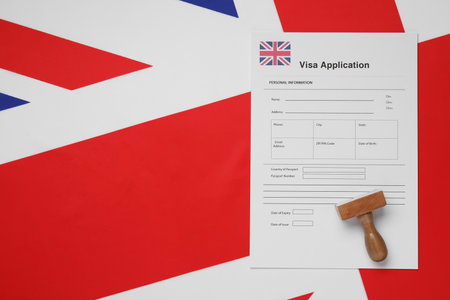 Immigration to the United Kingdom. Visa application form and wooden stamp on flag, top view. Space for textの写真素材