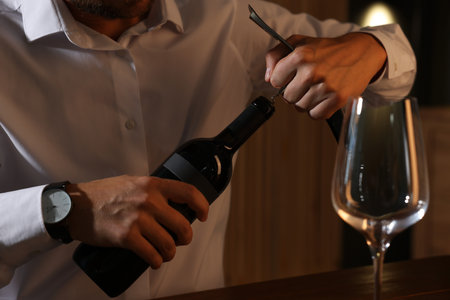 Romantic dinner. Man opening wine bottle with corkscrew at table indoors, closeupの写真素材