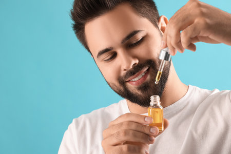 Handsome man with cosmetic serum in hands on light blue background, space for textの写真素材