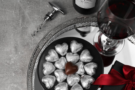 Bottle, glass of red wine, heart shaped chocolate candies, corkscrew and gift box on light gray textured table, above view. Space for textの写真素材
