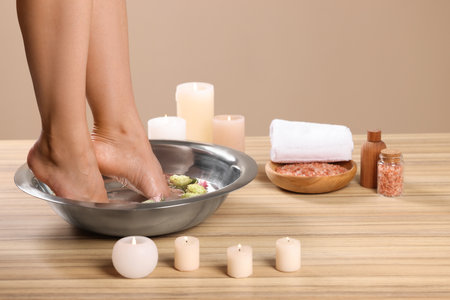 Woman soaking her feet in bowl with water and flowers on wooden surface, closeup. Pedicure procedureの写真素材