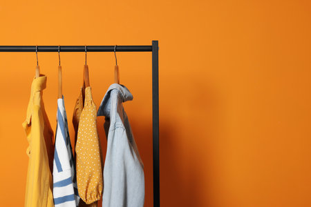 Rack with stylish clothes on wooden hangers against orange background, space for textの写真素材