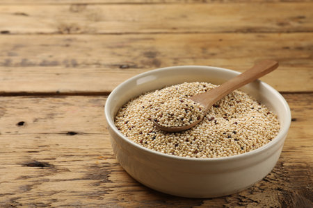 Raw quinoa seeds and spoon in bowl on wooden table, closeup. Space for textの写真素材