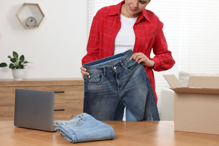 Young woman with just unpacked new jeans and laptop on wooden table indoors, closeup. Online shoppingの写真素材