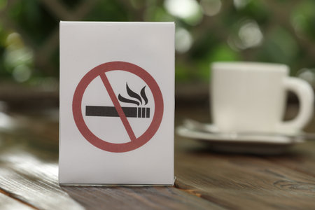 No Smoking sign and cup of drink on wooden table against blurred background, closeupの写真素材