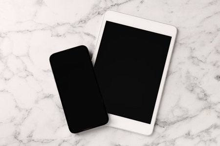 Tablet and smartphone with blank screens on white marble table, flat lay