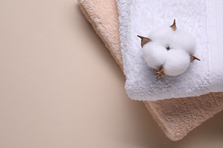Fluffy cotton flower and terry towels on beige background, top view. Space for textの写真素材