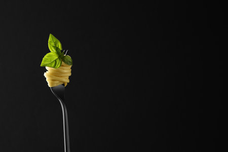 Fork with tasty pasta and basil on black background, space for textの写真素材