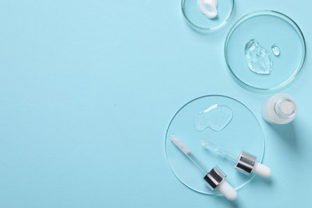 Petri dishes with samples of cosmetic serums, bottle and pipettes on light blue background, flat lay. Space for textの写真素材