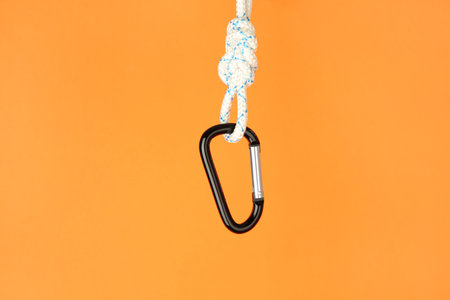 One metal carabiner hanging on rope against orange backgroundの写真素材