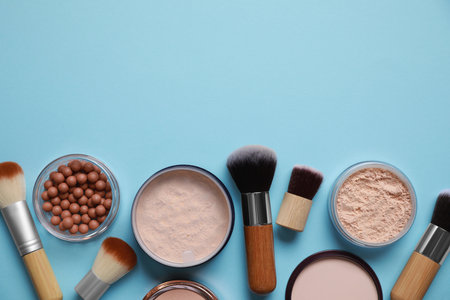 Different face powders and makeup brushes on light blue background, flat lay. Space for textの写真素材