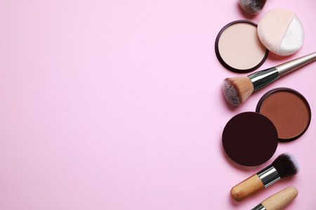 Different face powders and makeup brushes on pink background, flat lay. Space for textの写真素材