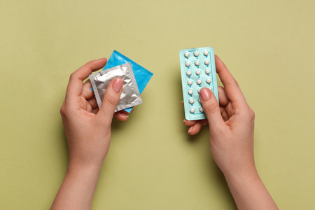 Woman with condoms and contraceptive pills on olive background, top view. Choosing birth control methodの写真素材