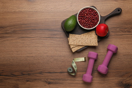 Healthy diet. Measuring tape, dumbbells and products on wooden table, flat lay. Space for textの写真素材