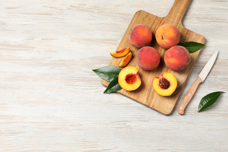 Fresh ripe peaches with green leaves and knife on light wooden table, top view. Space for text