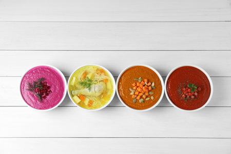 Tasty broth and different cream soups in bowls on white wooden table, flat layの写真素材