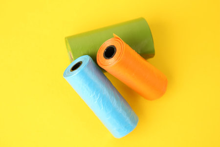 Colorful dog waste bags on yellow background, above view