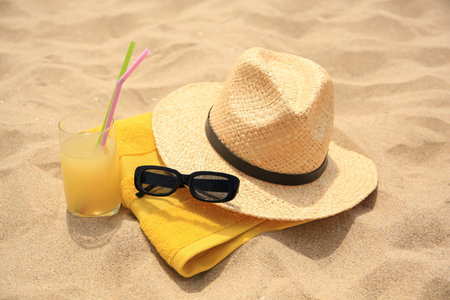 Straw hat, sunglasses, towel and refreshing drink on sand. Beach accessoriesの写真素材