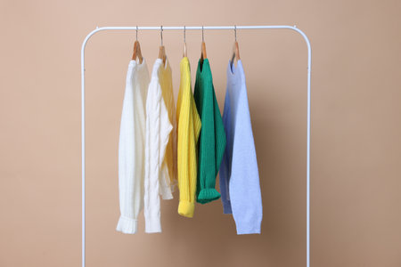 Rack with different warm sweaters on beige backgroundの写真素材