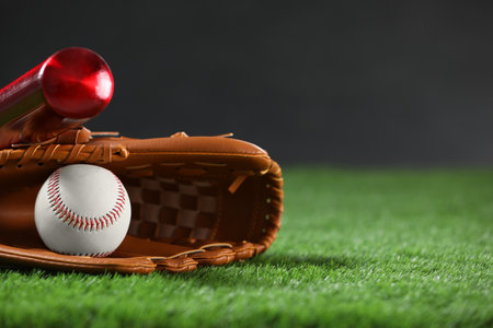 Baseball bat, leather glove and ball on green grass against dark background, closeup. Space for textの写真素材