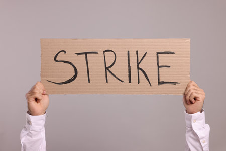 Man holding cardboard banner with word Strike on light gray background, closeupの写真素材