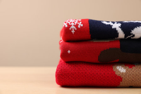 Stack of different Christmas sweaters on table against beige background. Space for textの写真素材