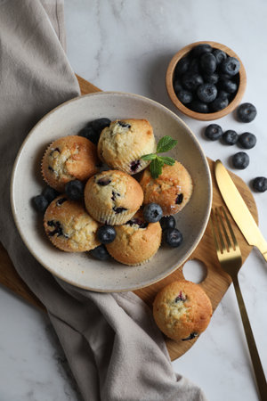 Delicious muffins with blueberries in bowl and cutlery on white marble table, flat layの写真素材