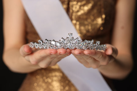 Woman in dress holding tiara on black background, closeup