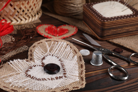 Heart shaped pieces of burlap fabric with different stitches and sewing tools on wooden table, closeupの写真素材