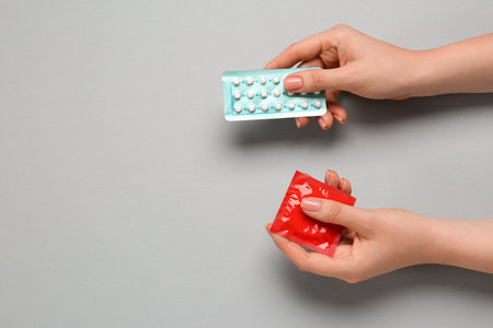Woman holding condom and contraceptive pills on gray background, top view with space for text. Choosing birth control methodの写真素材