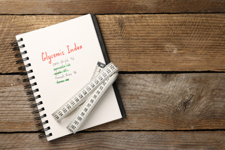 Glycemic Index. Notebook with information and measuring tape on wooden table, top view. Space for textの写真素材
