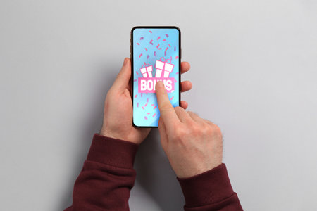 Bonus gaining. Man using smartphone on light gray background, top view. Illustration of open gift...