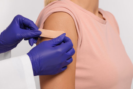 Nurse sticking adhesive bandage on woman's arm after vaccination on light background, closeupの写真素材