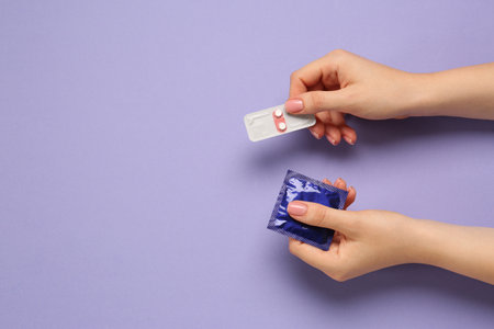 Woman holding condom and contraceptive pills on violet background, top view with space for text. Choosing birth control methodの写真素材
