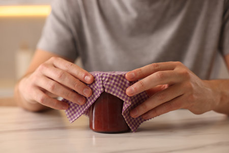 Man packing jar of jam into beeswax food wrap at light table indoors, closeupの写真素材