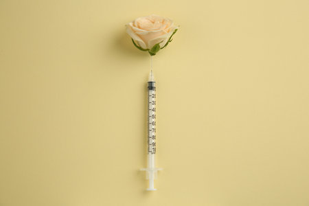 Medical syringe and beautiful rose on pale yellow background, top viewの写真素材