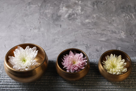 Tibetan singing bowls with water, beautiful chrysanthemum flowers on gray textured table. Space for textの写真素材