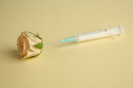 Medical syringe and beautiful rose on pale yellow background, closeupの写真素材