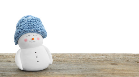 Cute decorative snowman in blue hat on wooden table against white background, space for textの写真素材