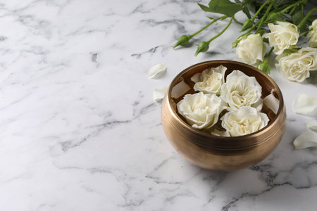 Tibetan singing bowl with water and beautiful roses on white marble table, space for textの写真素材