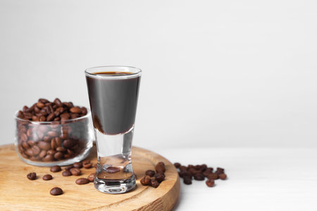 Shot glass of coffee liqueur and beans on white table, space for textの写真素材