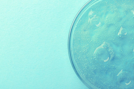 Petri dish with color liquid sample on light blue background, top view. Space for text