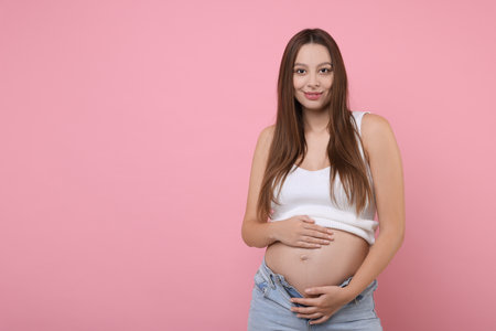 Beautiful pregnant woman with long hair on pink background, space for textの写真素材
