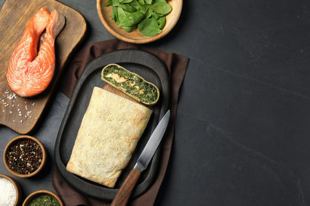 Flat lay composition of delicious strudel with salmon and spinach served on dark textured table. Space for textの写真素材