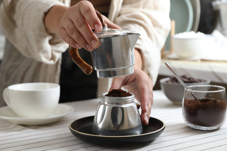 Brewing aromatic coffee. Woman with moka pot at table in kitchen, closeupの写真素材