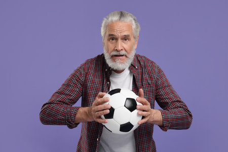 Senior sports fan with soccer ball on purple backgroundの写真素材