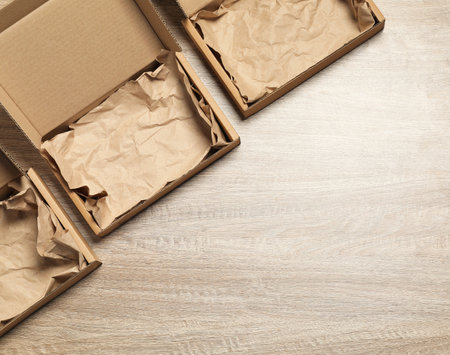 Open cardboard boxes with crumpled paper on wooden background, flat lay. Space for textの写真素材