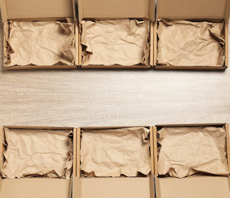 Many open cardboard boxes with crumpled paper on wooden background, flat lay. Space for text