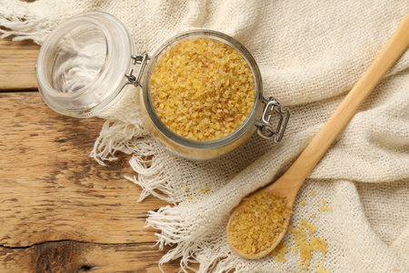 Glass jar and spoon with raw bulgur on wooden table, flat layの写真素材