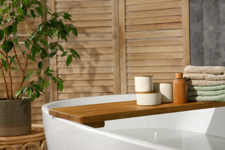 Wooden tray with spa products and towels on bath tub in bathroom. Space for textの写真素材